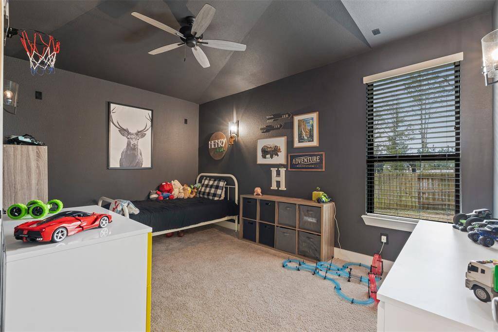 This is a cozy, well-lit bedroom with dark walls and carpeted flooring. A large window provides natural light and a view of the backyard.