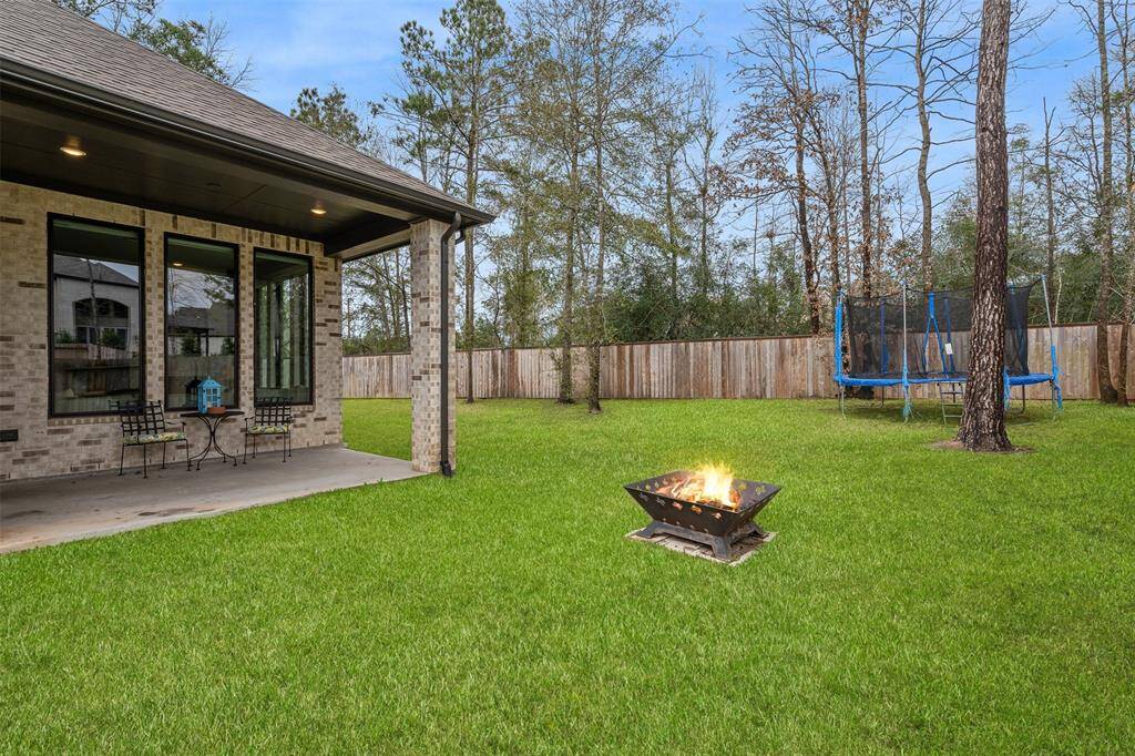 This backyard features a spacious lawn. The covered patio provides a cozy seating area, ideal for relaxation and outdoor entertaining. Surrounded by tall trees and a wooden fence, it offers privacy and a serene atmosphere.