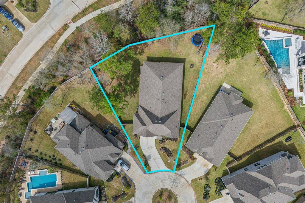 This aerial photo shows a house located in a cul-de-sac with a uniquely shaped lot outlined in blue. The property includes a spacious backyard, partly wooded.
