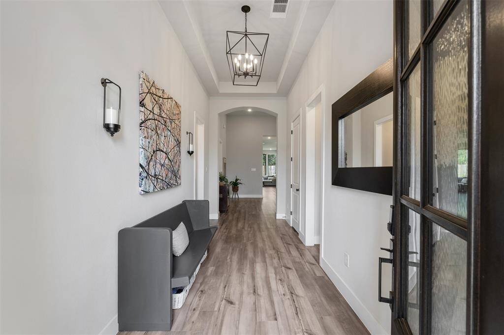 This inviting hallway features modern lighting, hardwood flooring. The space is bright, leading to an open, airy living area.