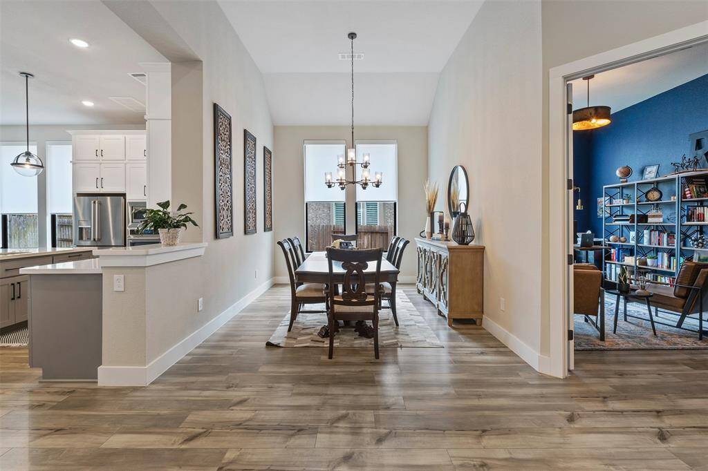 Spacious, open-concept dining area with elegant wood flooring and modern lighting. It seamlessly connects to a contemporary kitchen featuring stainless steel appliances.