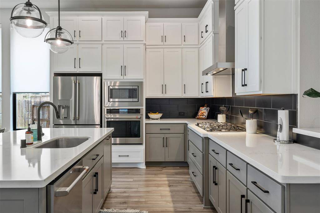 Modern kitchen featuring sleek white cabinetry, stainless steel appliances, and a central island with a sink. Bright and open with stylish pendant lighting and a black backsplash for contrast. Perfect for cooking and entertaining.
