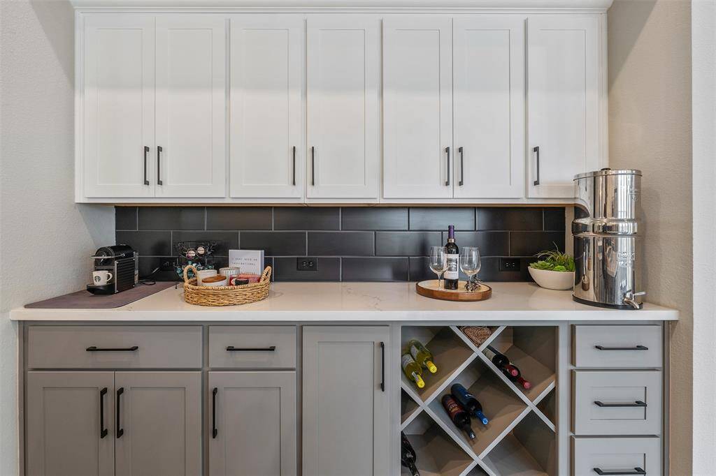 This modern kitchen nook featuring sleek cabinetry in a two-tone design. The area includes ample counter space, a wine rack, and a stylish backsplash, perfect for entertaining or a coffee station.