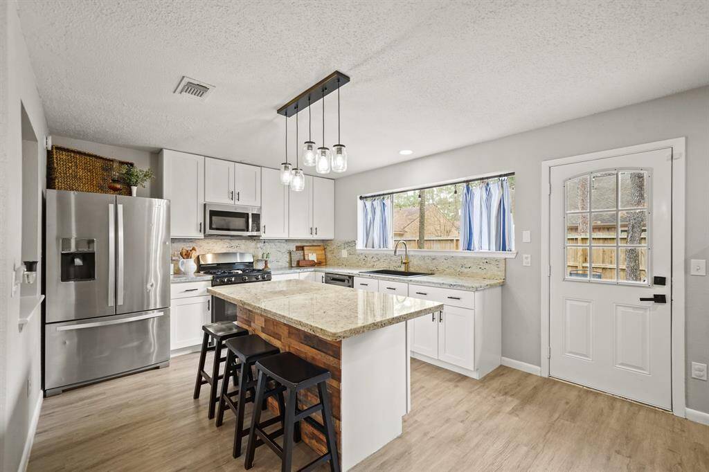 A granite surfaced island illuminated by pendant lighting has breakfast bar seating, doubles as a serving bar and provides additional prep & storage space.