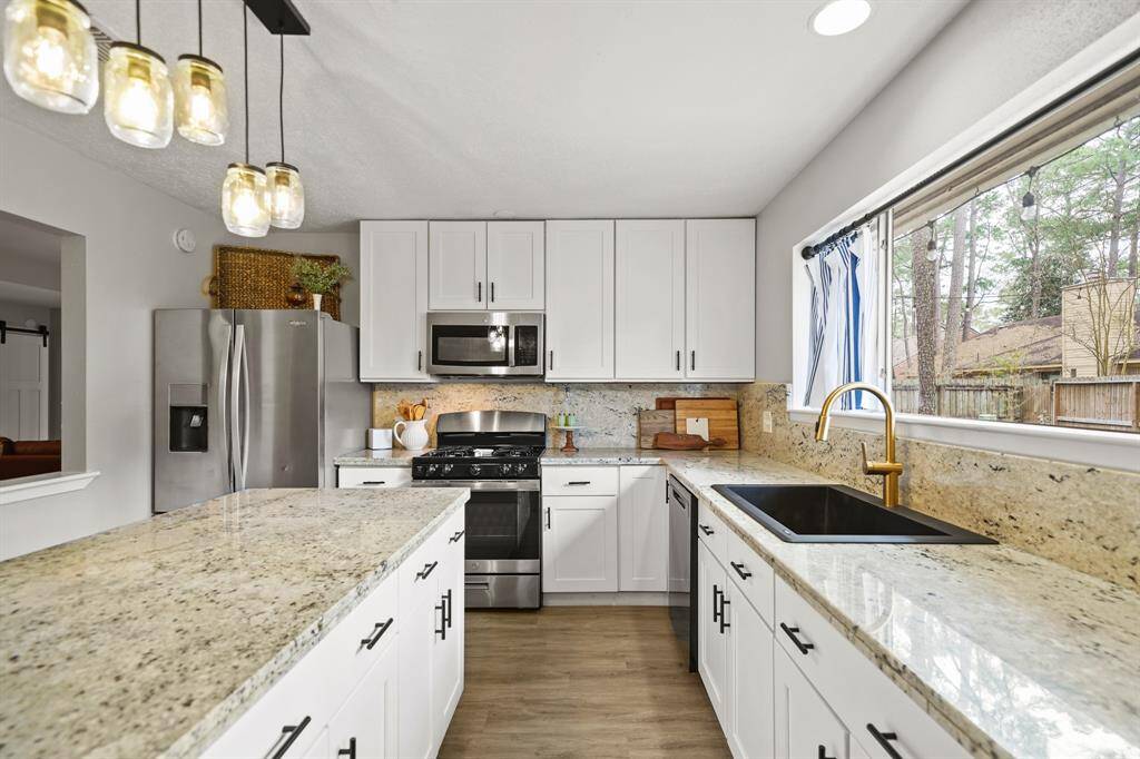 A composite granite single basin sink with gold plumbing fixtures & garbage disposer installed in 2022 sits just below a large window with recessed lighting & overlooks the backyard.
