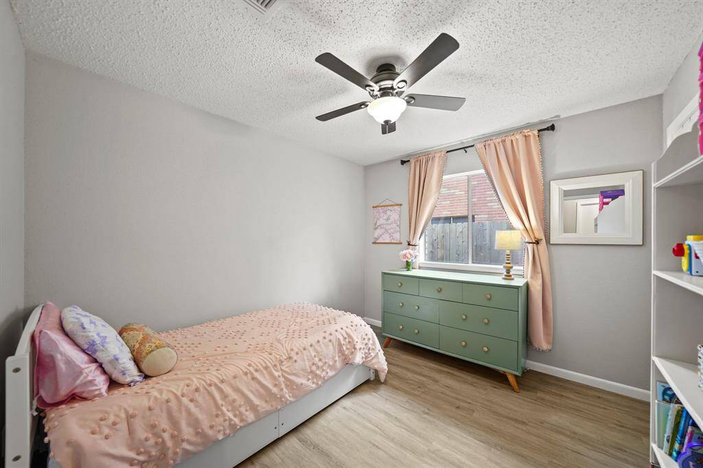 The secondary bedroom includes a ceiling fan with lighting, window with drapes overlooking the side yard & luxury vinyl plank hardwood floors.