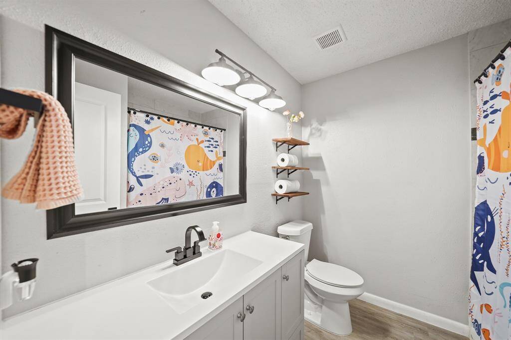 Located near the secondary bedrooms and convenient for guests, the home's second full bath has a painted cabinet supporting a solid surface counter top with integrated sink, a framed mirror with lighting above, a ceramic tile surrounded combinationt tub/shower & luxury vinyl plank hardwood floors.