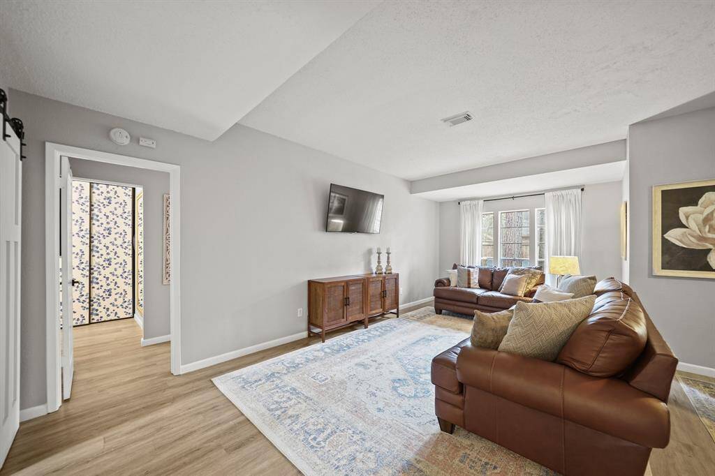 The living room is filled with natural light from the large windows with drapes overlooking the backyard. The owner's suite is accessible just through the entrance on the left.