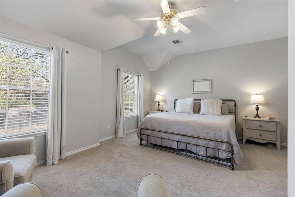 The spacious primary suite features neutral paint, a ceiling fan, and large windows that fill the room with abundant natural light.