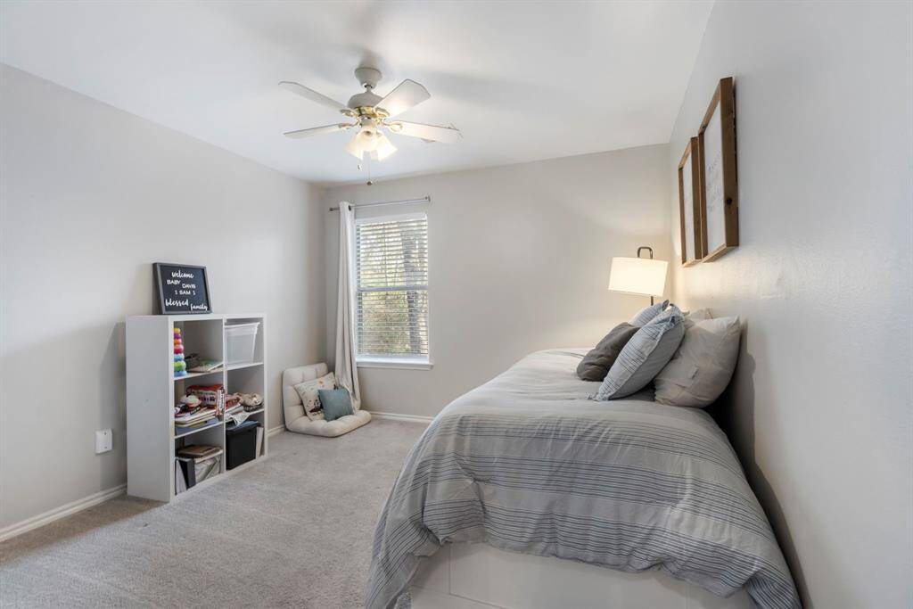 One of the two secondary bedrooms features carpet, neutral paint, a ceiling fan, and a large window, allowing for plenty of natural light.