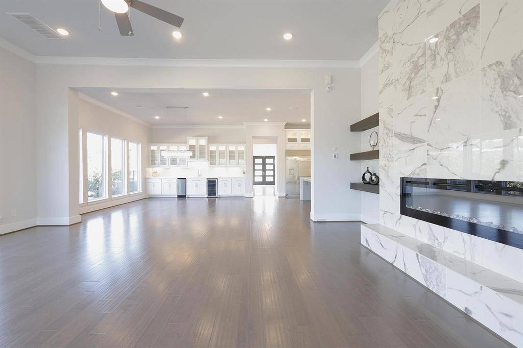 The elegant primary well-lit walk-in closet with ample shelving, hanging space, and a central  marble island for additional storage. The sleek, modern design features white cabinetry and a hardwood floor, creating a clean and organized look.