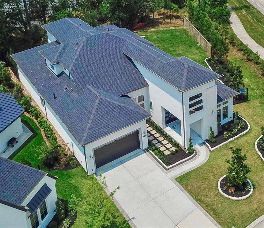 This  luxury modern home features a striking two-story entrance with large chandelier and large  windows, a sleek façade, and a well-maintained  lawn. The drive way offers ample space, and the overall design emphasizes clean lines and contemporary style.