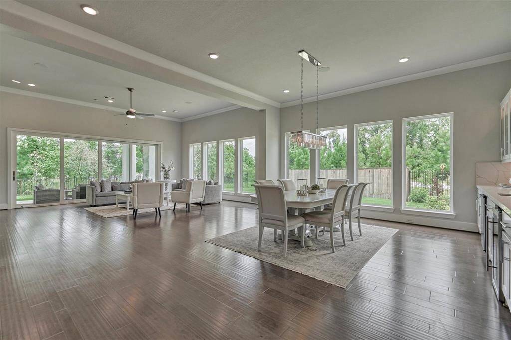 This  luxury modern open floor home features a striking two-story entrance with large chandelier and large  windows, a sleek façade, and a well-maintained  lawn. The drive way offers ample space, and the overall design emphasizes clean lines and contemporary style.