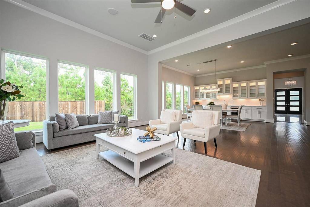 This spacious, open-concept living and dining area features large windows offering abundant natural light and views of the greenery outside. The room has elegant hardwood floors, a modern chandelier located in the dining room , and a a cozy seating area near sliding glass doors. Perfect for entertaining and family gatherings.
