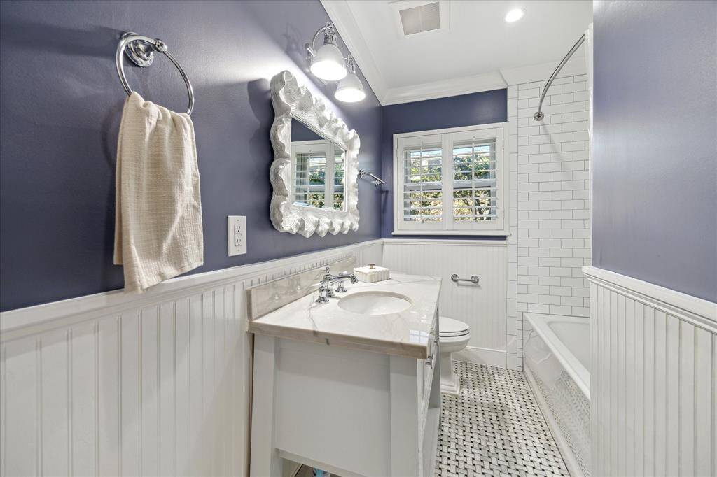 Updated hall bathroom with designer finishes, marble tile floor, custom wainscotting, subway tile bath, extra deep bathtub, custom vanity with quartzite marble countertop, plantation shutters and built in linen storage.