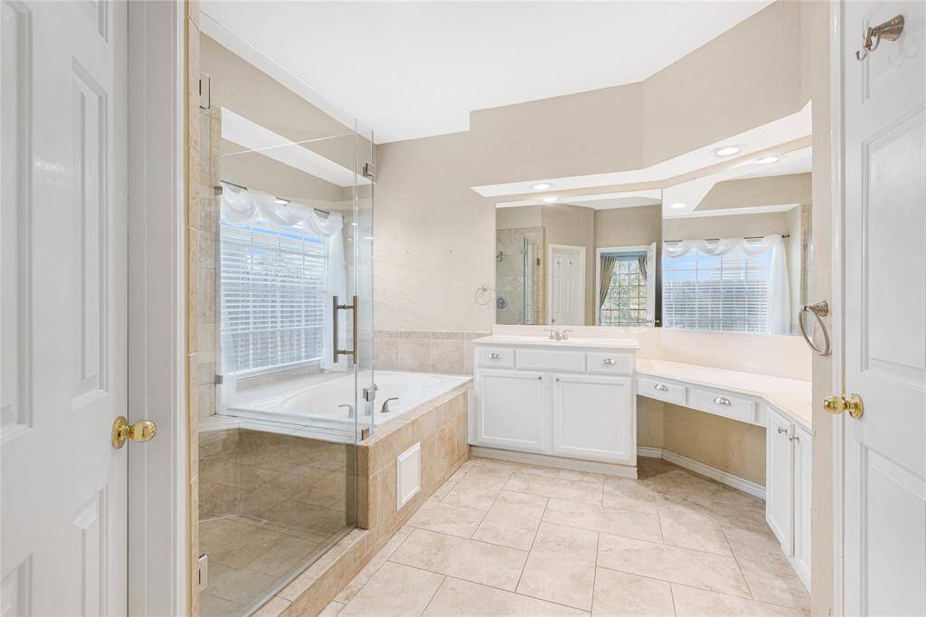 The spa-like primary en-suite bathroom features a large jetted tub, separate glass-enclosed shower, dual vanity with ample countertop space, and tiled flooring