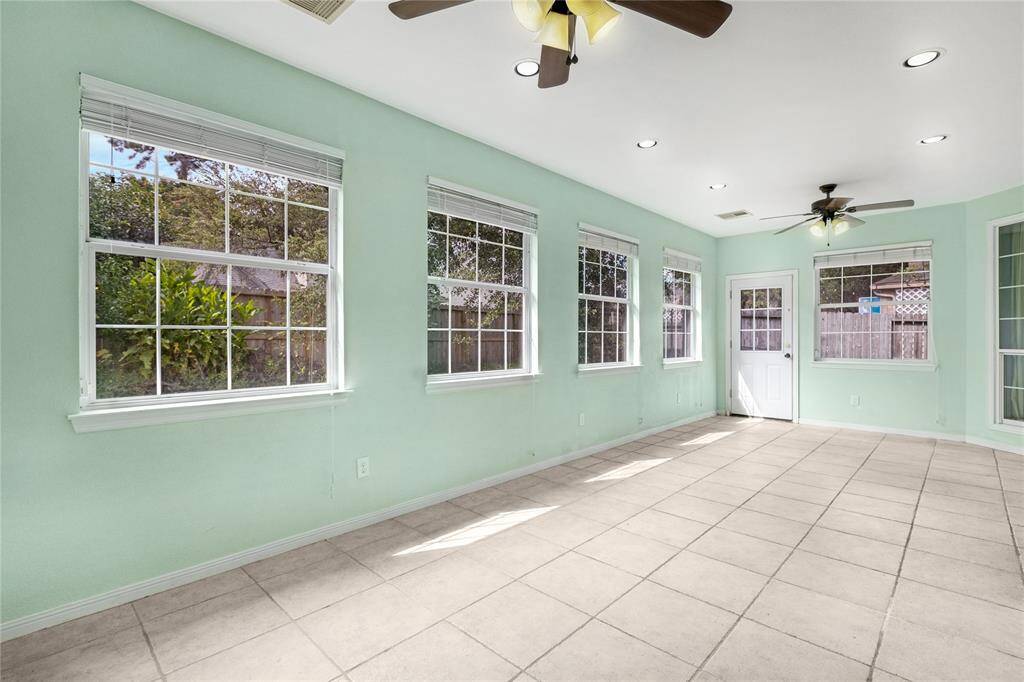 Bright and airy, this sunroom features large windows for plenty of natural light, tile flooring for easy maintenance, and a ceiling fan for comfort. It offers direct access to the backyard through a glass door.