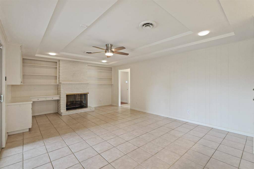 Den with built ins and tray ceiling with ceiling fan and recessed lighting.
