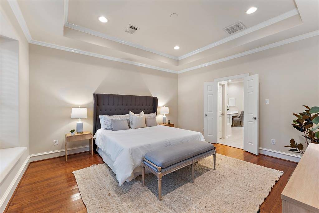 A refined primary suite with tray ceilings, tasteful crown molding, and expansive windows that invite natural light. Hardwood floors complement the room’s airy ambiance, underscoring a tranquil sense of luxury.