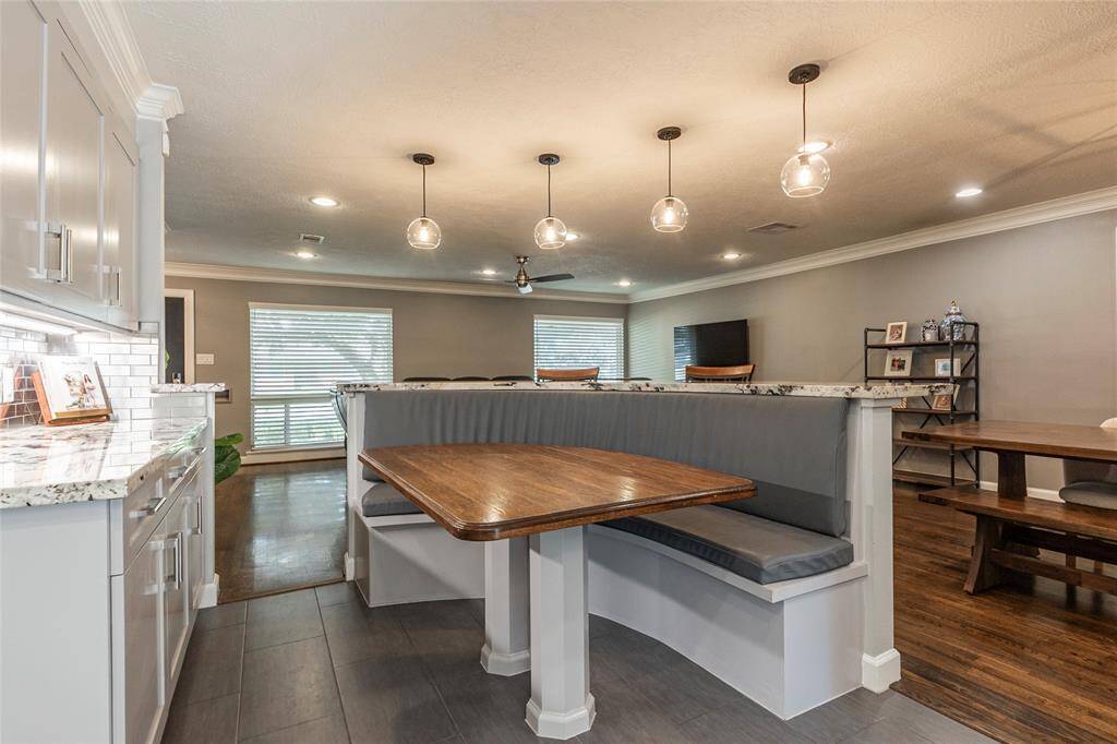This spacious kitchen and dining area features modern pendant lighting, a cozy built-in breakfast nook with a wooden table, and sleek cabinetry with granite countertops. The open layout flows into the living area, creating a bright and inviting space perfect for gatherings.