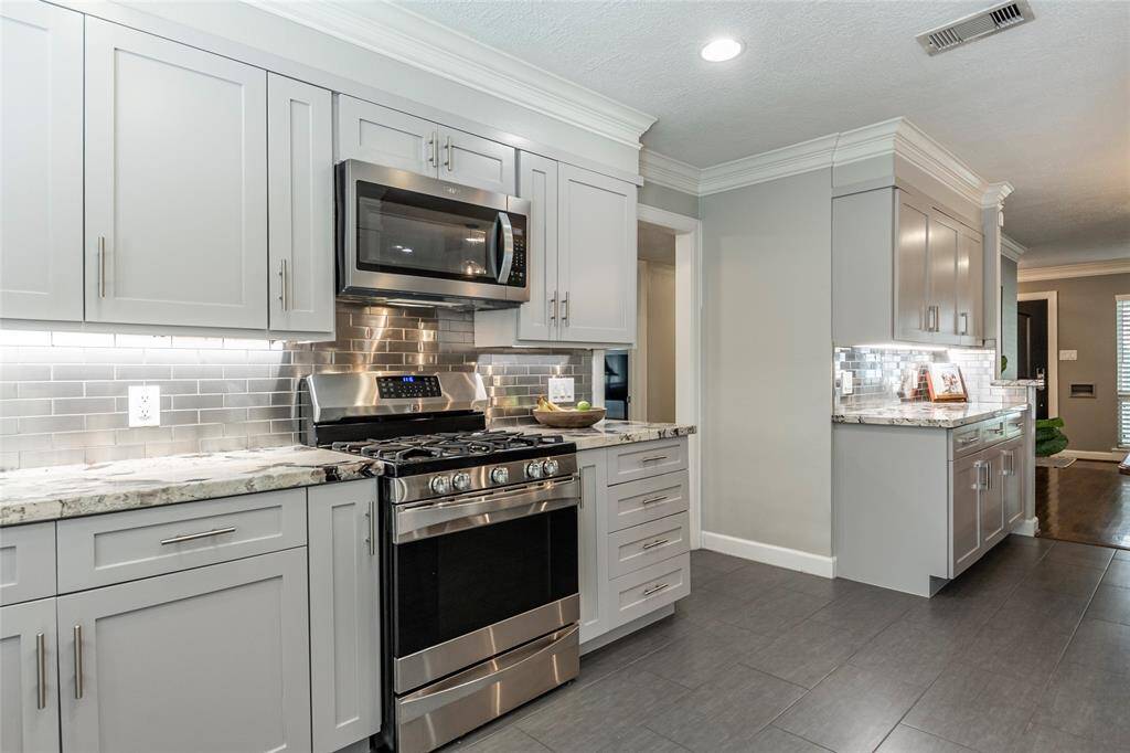 This kitchen features modern gray cabinetry, stainless steel appliances, and a sleek tile backsplash. The countertops are gorgous granite, and there's ample lighting for a bright, inviting space.