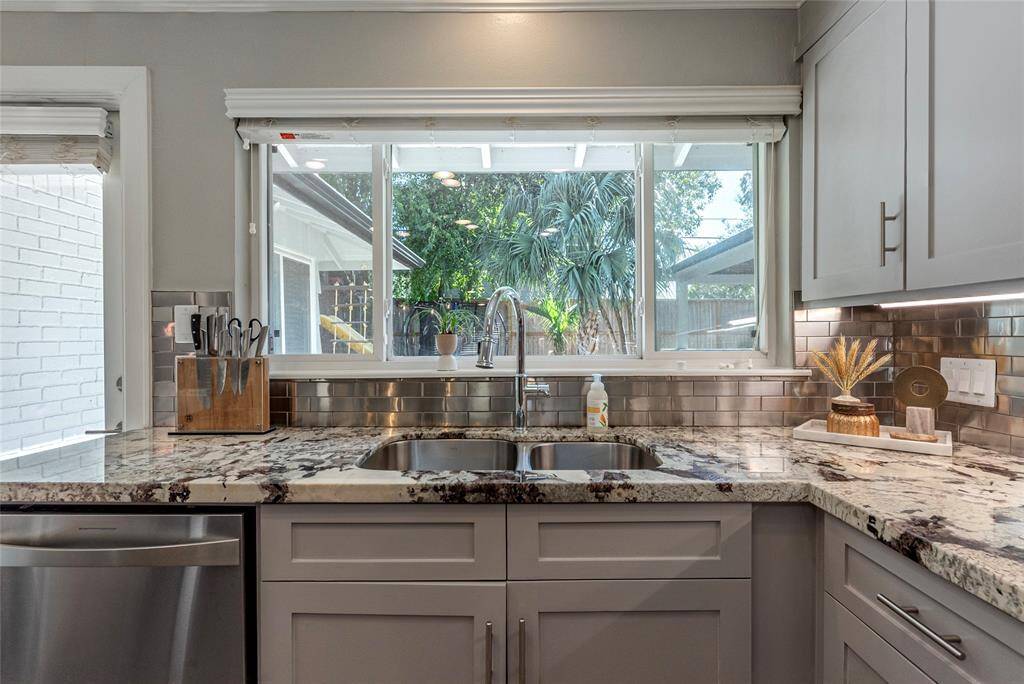 This kitchen features granite countertops, a double sink, and modern cabinetry. A large window provides natural light and views of the backyard, while stainless steel appliances add a sleek touch.