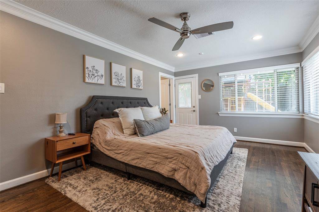 The primary bedroom features a cozy design with ample natural light from large windows. The wooden floors and neutral color palette create a warm and inviting atmosphere.