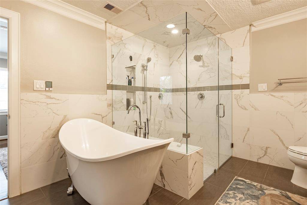 Primary bathroom features a freestanding bathtub and a spacious glass-enclosed shower with elegant walls. The neutral tones and sleek fixtures create a luxurious and relaxing atmosphere.