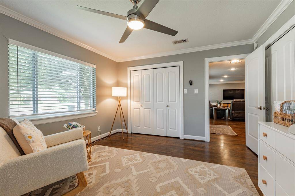 This bedroom features a cozy, well-lit space with a large window, neutral walls, and hardwood floors. It includes a ceiling fan, a closet with double doors, and an open layout leading to a living area. The decor is modern and inviting, perfect for a home office or reading nook.