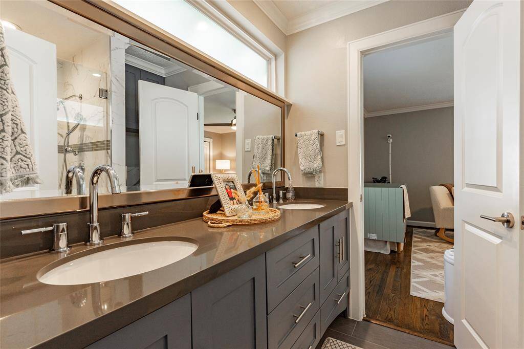 Secondary bathroom with a double sink vanity, sleek countertops, large mirrors, and neutral tones. The space is well-lit and opens into a cozy room with hardwood flooring.