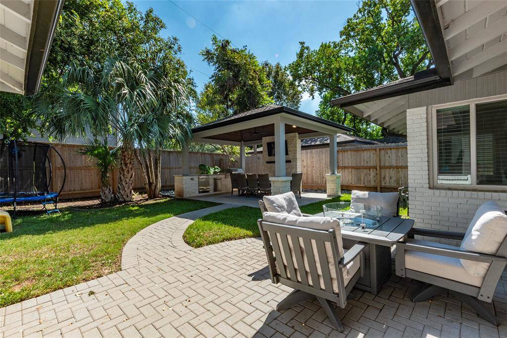 This backyard features a spacious patio with comfortable seating, a covered outdoor dining area, and a built-in grill station, perfect for entertaining. The space is surrounded by a privacy fence and lush greenery, creating a serene oasis.