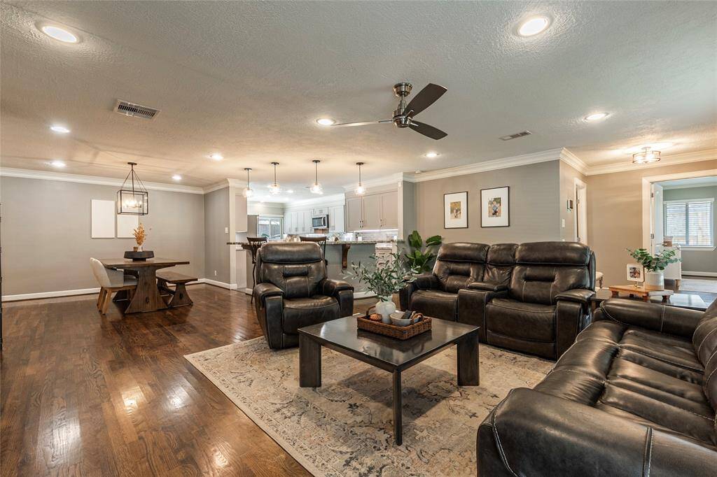 This spacious living area features elegant hardwood floors, stylish recessed lighting, and a modern ceiling fan. The open layout seamlessly connects to a contemporary kitchen with a breakfast area and dining space, creating a perfect setting for entertaining.