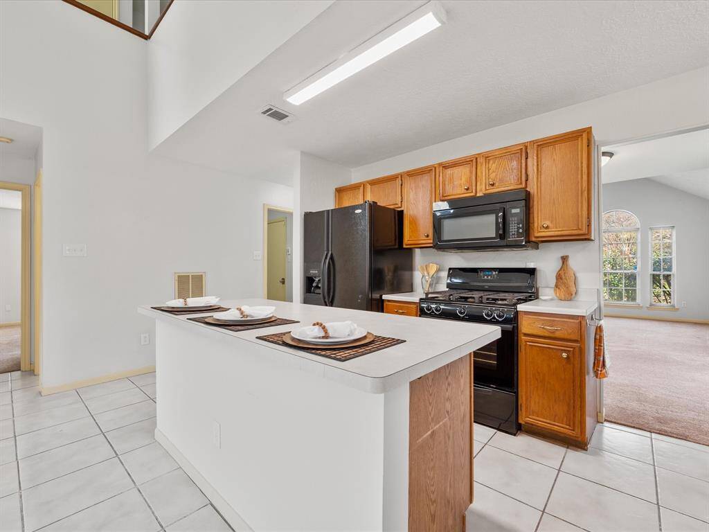 The kitchen features an island and wooden cabinets. It opens to a second living space.