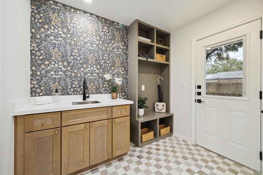 THE UTILITY ROOM BOASTS A BUILT-IN MUD AREA, KARMEL CABINETS WITH SINK, AND DESIGNER-PICKED WALLPAPER. THE BACKDOOR LEADS TO THE BACKYARD.