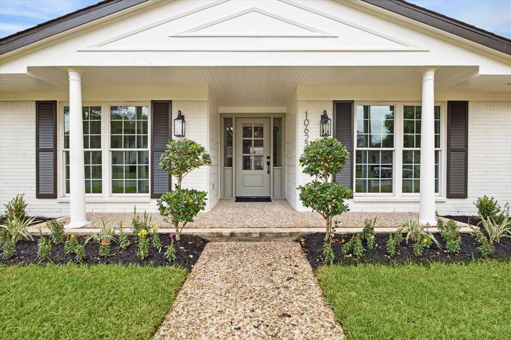 THE HOME FEATURES A LARGE COVERED PATIO WITH PILLARS AND GABLED ROOF. NOTICE THE RECENT PROFESSIONAL LANDSCAPING WITH FLOWERING SHRUBS AND MANICURED BUSHES.