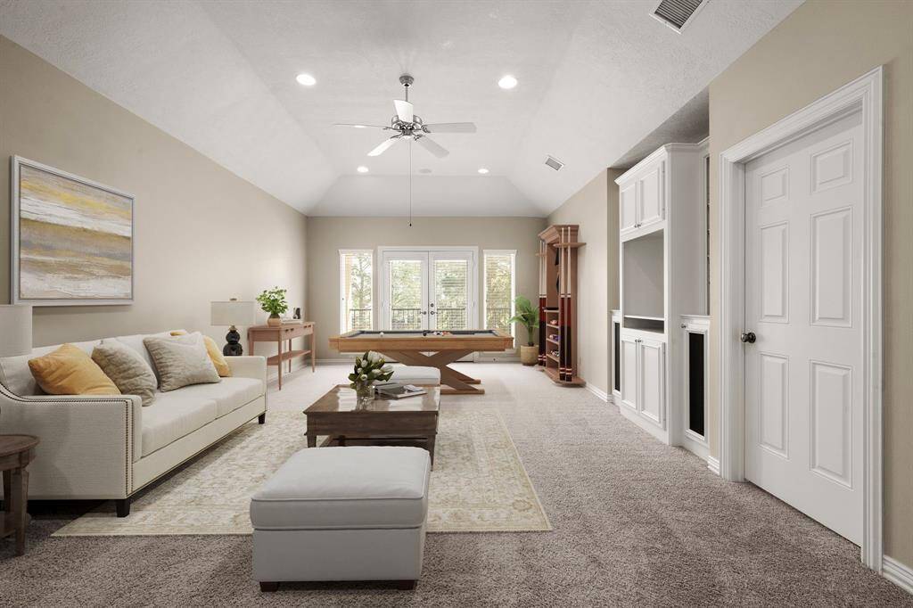This spacious game room features high ceilings with recessed lighting and a ceiling fan. It includes built-in shelving and a storage area, with large windows and a glass door leading to a balcony, offering plenty of natural light.