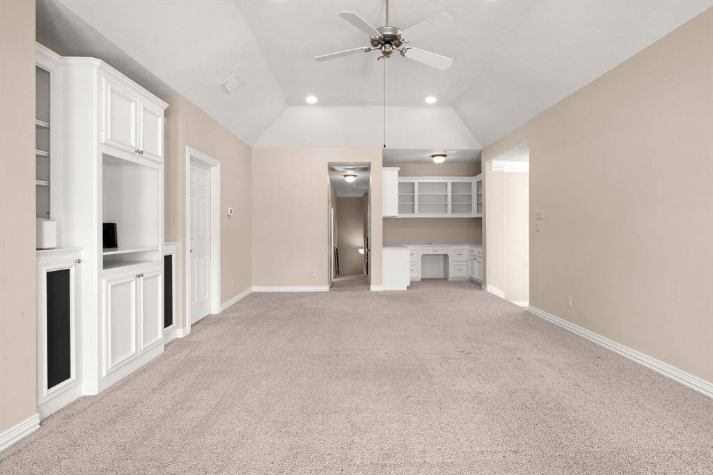 The game room has neutral tones, featuring built-in white cabinetry and shelving. It includes a ceiling fan and recessed lighting, with a built-in desk area perfect for a home office, study or homework space.