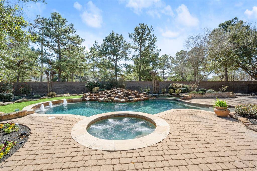 The backyard features a spacious pool with a waterfall, surrounded by a well-maintained stone patio and lush greenery, providing a serene and private outdoor retreat.