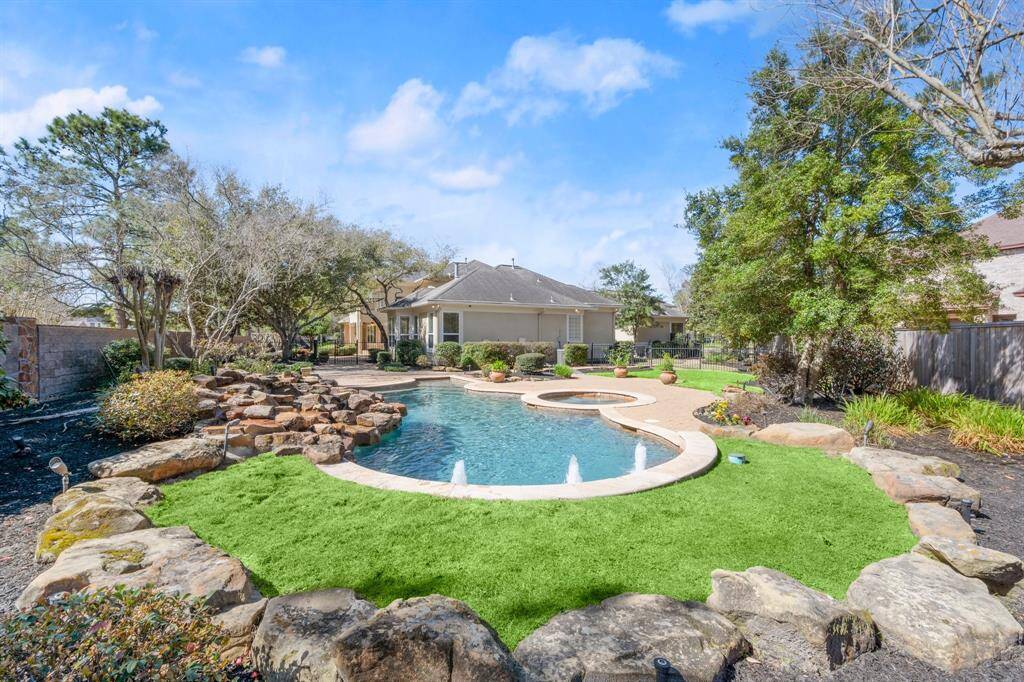 Spacious backyard featuring a beautifully landscaped pool with a rock waterfall, surrounded by lush greenery and mature trees, ideal for relaxation and entertaining.