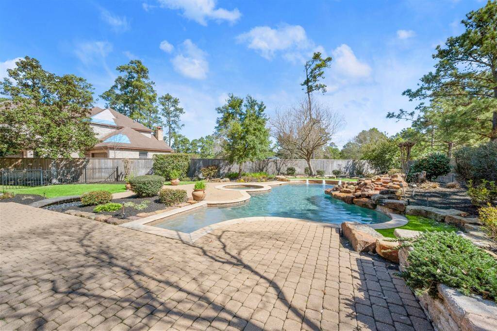 This backyard features a spacious, landscaped area with a luxurious pool surrounded by stone accents and greenery. It offers a peaceful retreat with ample space for outdoor entertaining.