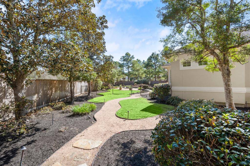 Beautifully landscaped backyard with a winding path, lush greenery, and mature trees. It features a well-maintained lawn, bordered by a wooden fence, leading to a gated area that enhances privacy and charm.