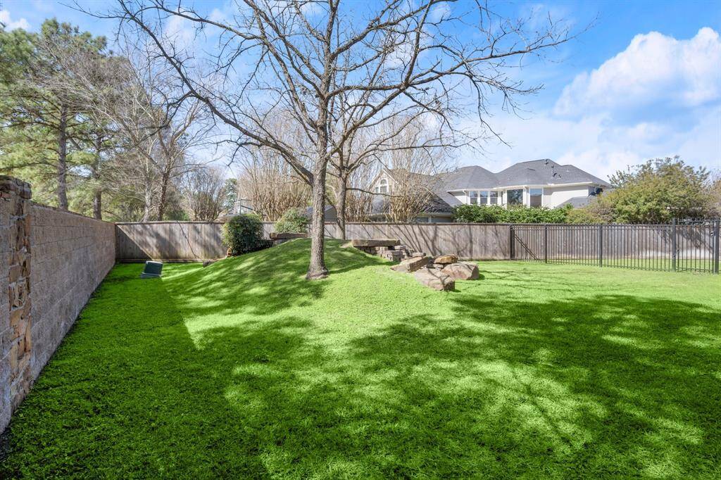 Spacious backyard with lush green grass, mature trees, and a mix of wooden and wrought iron fencing for privacy. Ideal for outdoor activities and relaxation. There's also a hidden space out here so be sure to look for it when you visit.