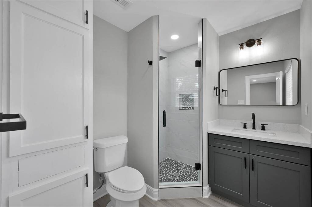 Primary bathroom features a luxurious shower, floor to ceiling storage cabinetry, and a quartz countertop with modern transitional fixtures. The shower is complete with a frameless glass shower door and a LARGE rain head shower fixture along with a secondary sprayer.