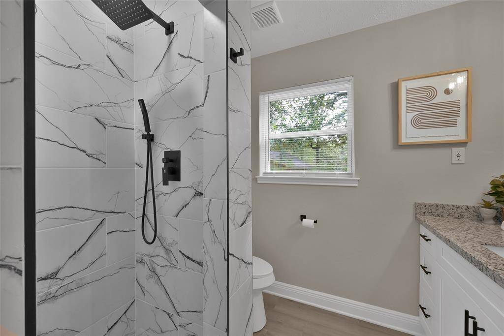 The bold black shower fixtures, featuring a rain head and handheld sprayer, beautifully complement the refined marble-veined tile.
