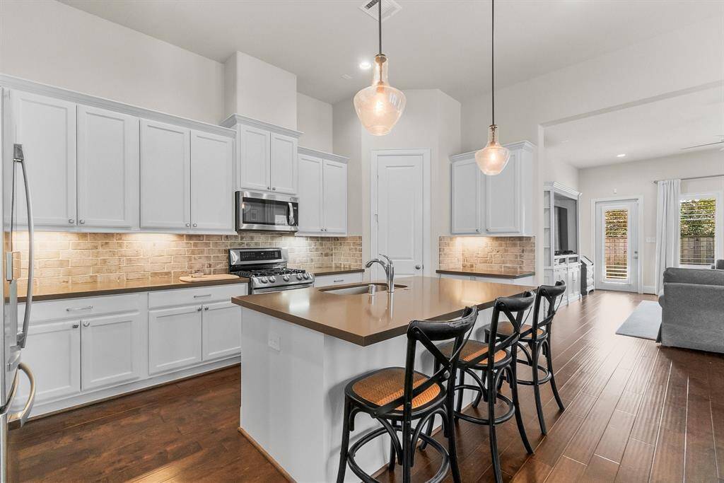 This kitchen features sleek white cabinetry, a stylish brick backsplash, and modern stainless steel appliances.