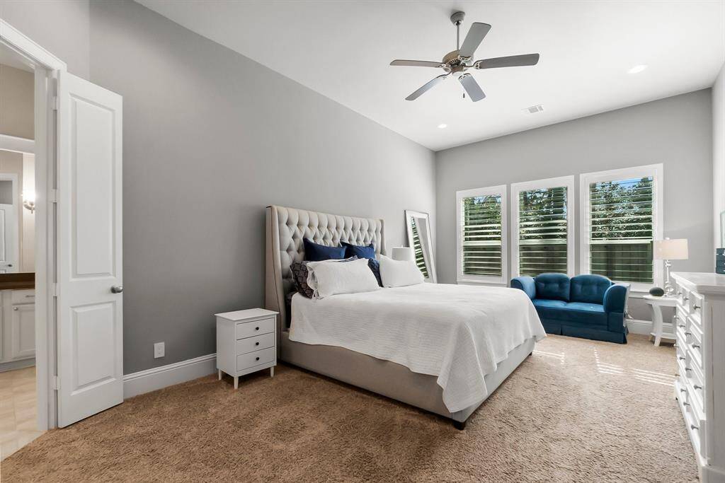 Primary bedroom has ample natural light from three windows with shutters, neutral-colored walls, and carpet for comfort.