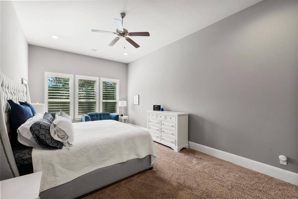 Primary bedroom with soft gray wall, carpeted flooring and classic shutters.