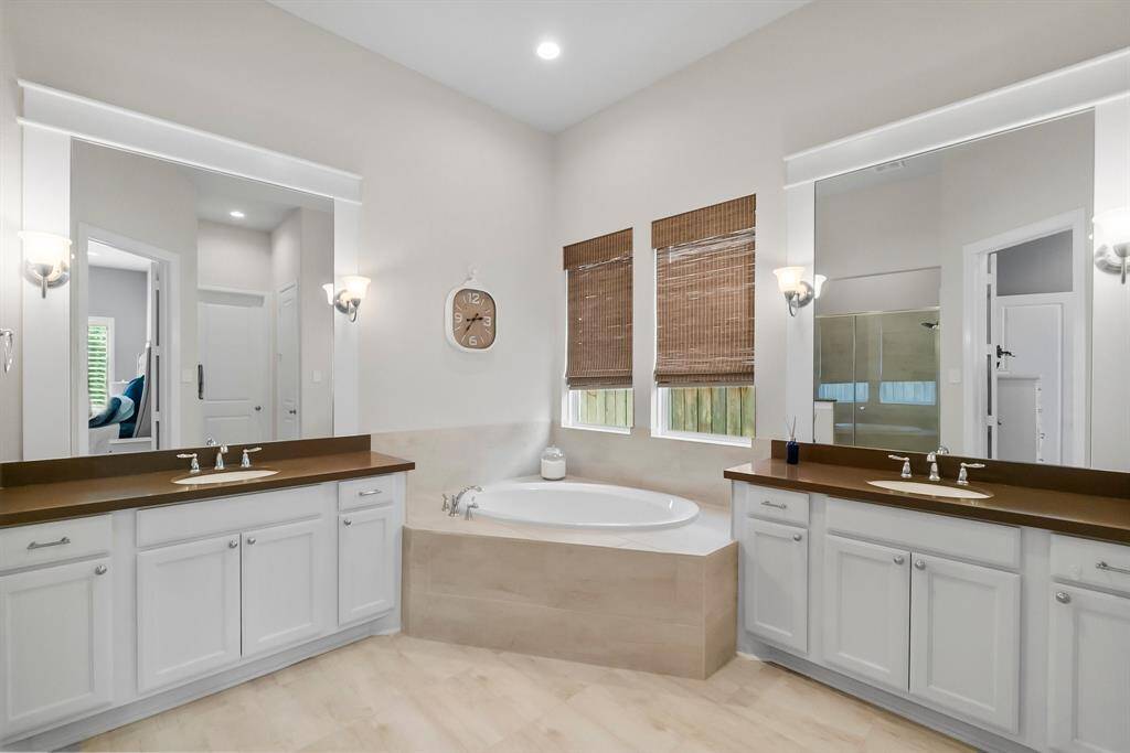 Primary bathroom features dual vanities with ample storage, a central soaking tub, and large windows with natural light.