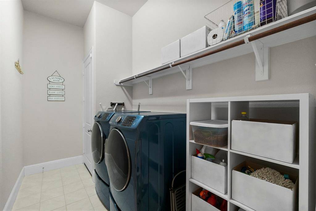 Well-organized utility room featuring a modern washer and dryer, ample shelving for storage, and a clean, bright design with tiled flooring.