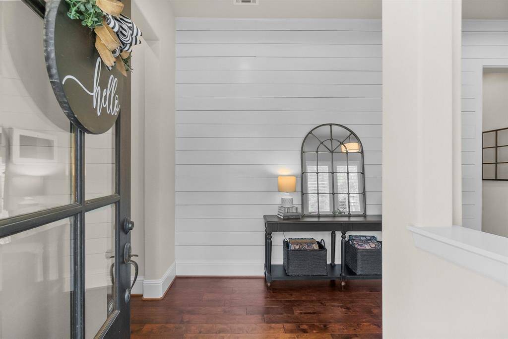 Entryway with a glass front door with interior  white shiplap walls set against rich wood flooring.